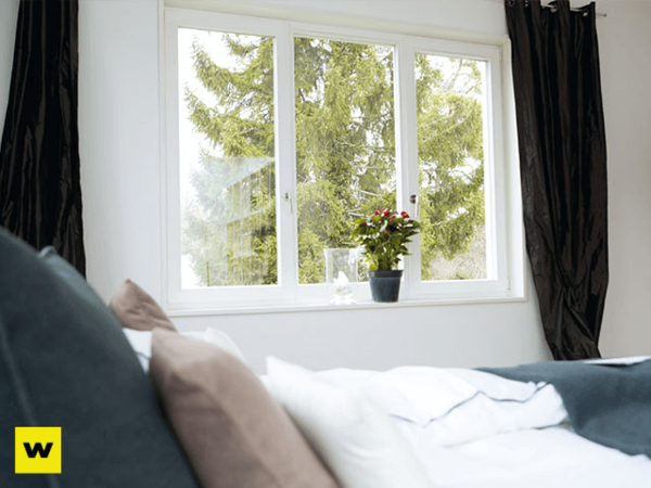 Helles Schlafzimmer mit großem Fenster, Bett und Zimmerpflanze für gemütliches Wohnen.