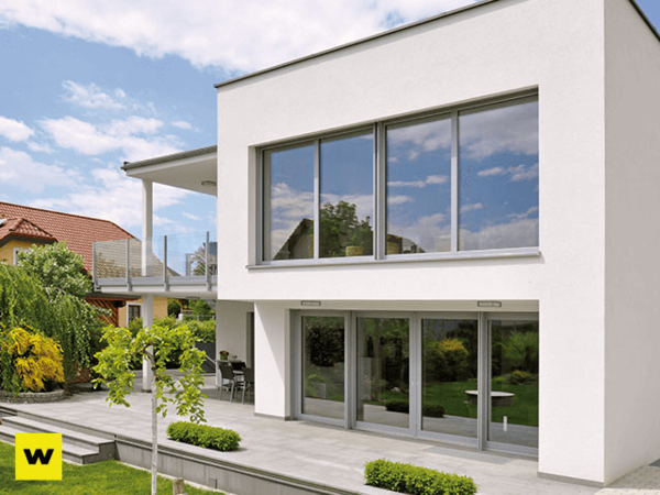 Modernes Einfamilienhaus mit großer Terrasse, bodentiefen Fenstern und Garten bei Sonnenschein.