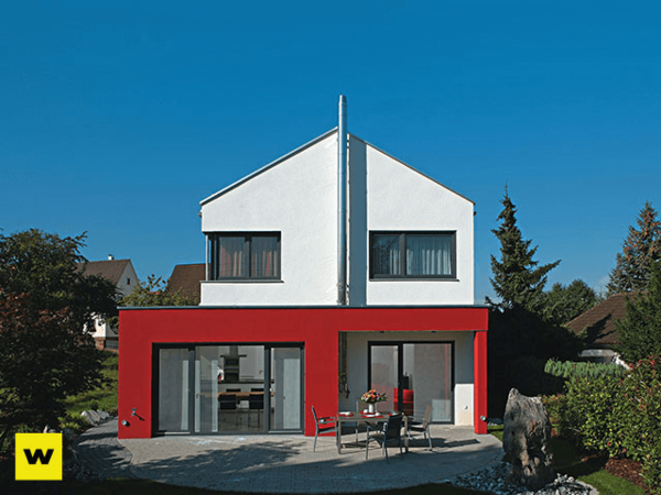 Modernes Einfamilienhaus mit roter Fassade, großen Fenstern und Garten bei Sonnenschein.